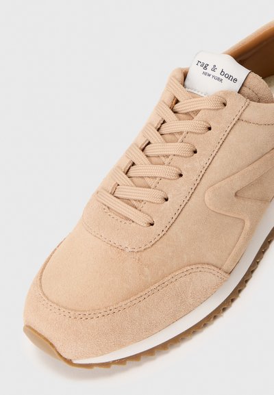 Beige ruskinds sneakers med rund tå, snørebånd foran og hvid sål. Har diskret syninger og et mærke med "rag & bone" branding.