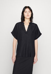 Top corto nero a maniche corte con scollo a V e vestibilità rilassata. Il tessuto ha una texture liscia e una leggera lucentezza, progettato per comfort e facilità.