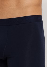 Marinblå herrboxershorts med en mjuk elastisk midjeband där "HANRO" är präglat, tillverkade av ett glansigt bomullsblandningsmaterial.
