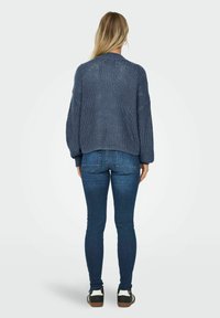 Blå stickad tröja med ribbad textur, sänkta axlar. Försedd med mörkblå slim-fit jeans och svarta sneakers med vita detaljer.