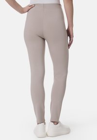 Beige Leggings aus einem glatten, dehnbaren Stoff, mit hohem Bund und taillierter Passform, kombiniert mit weißen Sportschuhen.