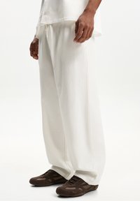 Vita, texturerade vida byxor med dragsko i midjan, i kombination med mörkbruna sportskor med snörning.