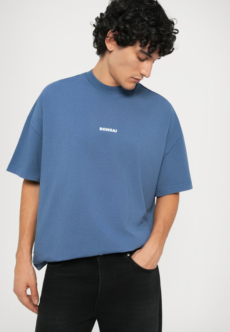 Blue cotton t-shirt with a relaxed fit, short sleeves, and a crew neckline. Features a white "BONSAI" logo on the chest.
