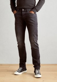 Jean slim noir et gris avec un bouton classique, poches avant et une texture délavée. Associé à des baskets en toile noires et blanches.