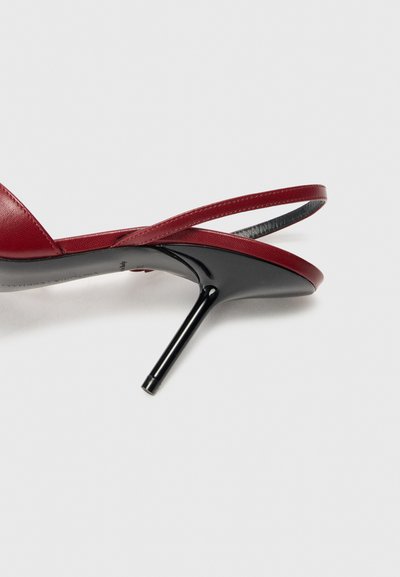 Sándal de tacón alto de cuero rojo con tacón stiletto negro, que presenta delgadas correas cruzadas y una textura suave.