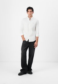 Camisa blanca de botones con mangas remangadas, combinada con jeans de mezclilla oscura. Líneas limpias, sin patrones visibles, llevada con calzado negro.