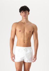 Shorts de bain blancs avec une taille élastique, fermeture à cordon et en tissu léger. Longueur courte et texture lisse.