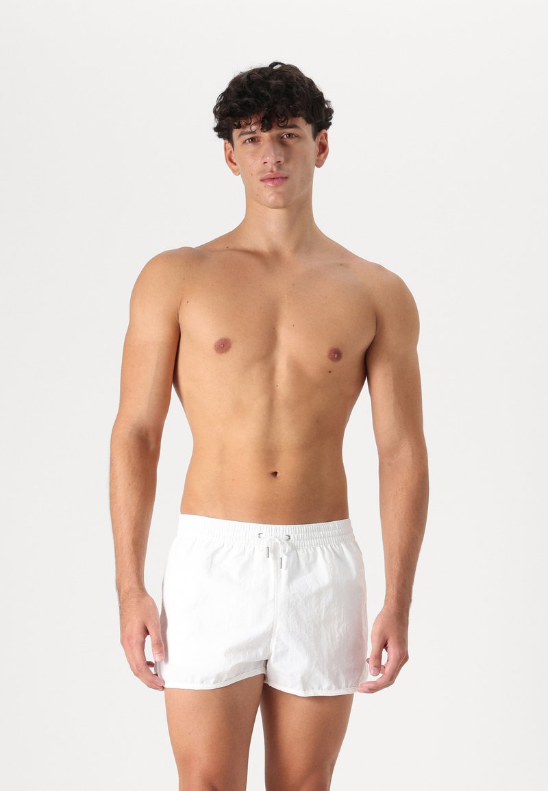 Shorts de bain blancs avec une taille élastique, fermeture à cordon et en tissu léger. Longueur courte et texture lisse.