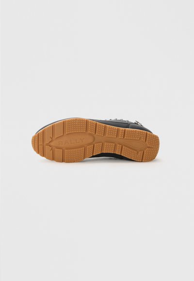 Zwarte sneaker met een gestructureerd leren bovenwerk, bruine rubberen buitenzool en zichtbare branding. Beschikt over een vetersluiting en decoratieve studs.