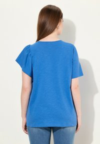 Modré tričko s krátkým rukávem a kulatým výstřihem, s nařaseným detailem na levém rameni a volným střihem.
