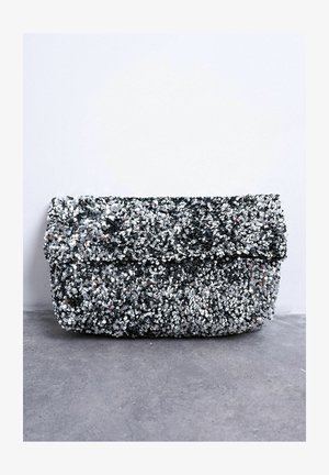 Kleine rechthoekige zilveren pailletten clutch met overslag, liggend op een grijze betonnen ondergrond tegen een witte achtergrond.