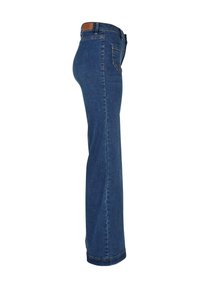 Jean bleu taille haute à jambe droite, montré de côté avec poche arrière visible et écusson de cuir de la marque sur la ceinture.