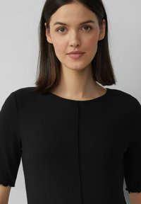 Zwarte ribbed T-shirt met korte mouwen, een ronde halslijn en golvende mouwranden, met een centrale naden detail. Glad textuur.