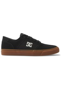 Svarta kanvas sneakers med gummisulor, med snördesign och en vit DC-logotyp på sidan. Slät textur, låg profil.