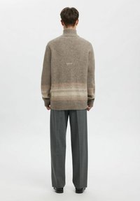 Beige, oversized genser med ribbet polokrage og flerfargede, horisontale striper nær kanten. Brukes med grå, skreddersydde bukser med vide ben.