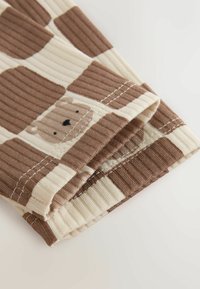 Close-up of folded ribbed fabric with brown and cream checkered pattern and a small bear face design on one square.