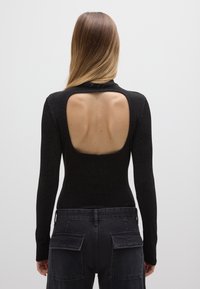 Schwarzer langärmliger Body mit Ausschnitt am Rücken, der eine strukturierte metallische Oberfläche und eine figurbetonte Silhouette aufweist, kombiniert mit dunklen Cargo-Hosen.