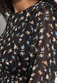 Svart blommig blus gjord av lättviktigt tyg. Har blå och rosa blommönster, texturerade ränder och detaljer med elastisk midja.