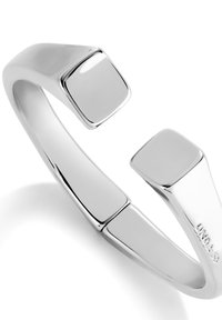 Pulsera de brazalete de plata con un acabado suave y pulido, que presenta dos extremos en forma de cuadrado y un diseño curvo y abierto.