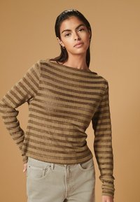 Langærmet top i brun med kontrasterende horisontale striber, letvægts tekstureret stof og en bred halsudskæring. Sammen med lyse beige bukser.