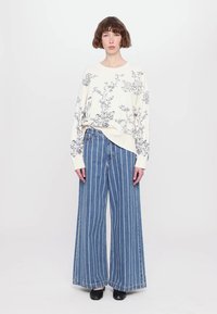 Off-white sweatshirt with black floral pattern, paired with wide-leg blue striped jeans and black shoes. Smooth fabric and casual design.