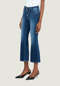 Jeans blu a vita alta, cropped, con un lavaggio sbiadito, chiusura anteriore con cinque bottoni e design classico a cinque tasche. Indossate con tacchi neri a punta.