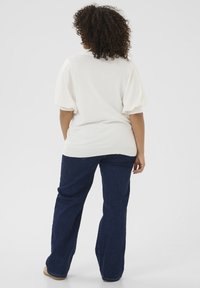 White knitted top with puff sleeves, paired with dark blue wide-leg jeans. Background is plain white. No visible patterns or hardware details.