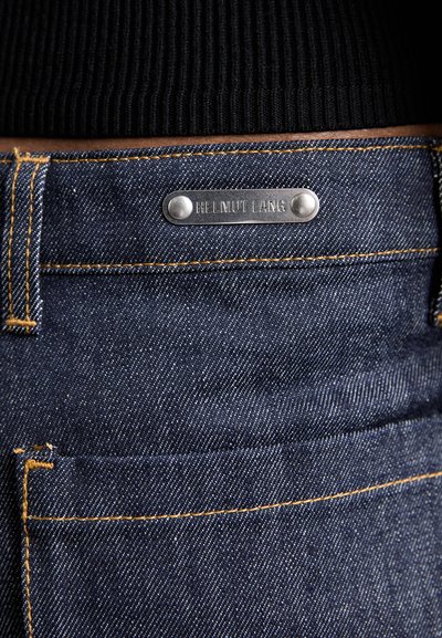 Jeans din denim albastru închis cu un tag metalic argintiu vizibil gravat "HELMUT LANG," accentuate de cusături aurii și un buzunar din spate.