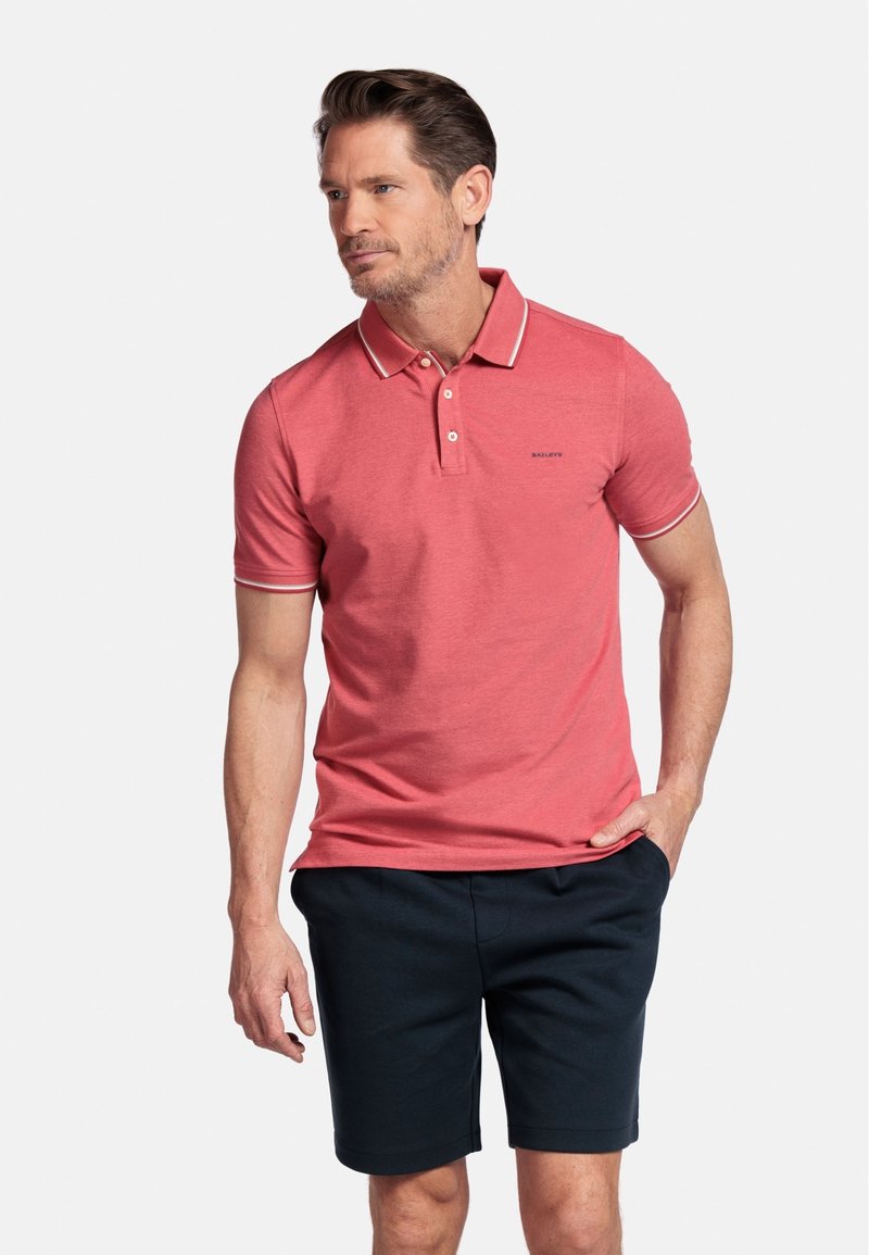 Rode poloshirt met witte kraagafwerking en logo, gecombineerd met donkerblauwe shorts. De stof lijkt glad en casual, geschikt voor warm weer.