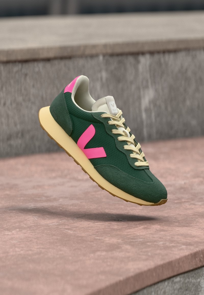 Πράσινο αθλητικό παπούτσι με ροζ λεπτομέρειες, με εξωτερικό από υφασμάτινο πλέγμα, κλείσιμο με κορδόνια και μπεζ λάστιχο σόλας.