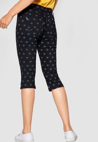 Svarta korta byxor med ett subtilt geometriskt mönster i vitt, tillverkade av mjukt tyg. Har en figursydd design och medelhög midja.