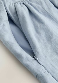 Manche en lin bleu clair avec une fermeture éclair fermée et un poignet élastique, montrant la texture du tissu et les détails des coutures.