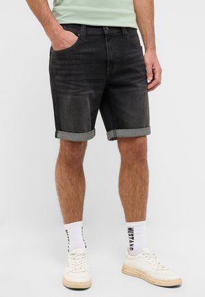 Dark wash denim shorts with rolled cuffs, featuring front pockets and a classic fit. Paired with white sneakers and patterned socks.