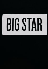 Czarne tło z białą prostokątną etykietą, na której znajduje się pogrubiony czarny napis „BIG STAR” wyśrodkowany w prostokącie.