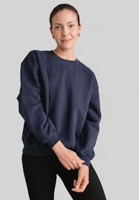 Granatowa bluza z okrągłym dekoltem wykonana z miękkiego materiału, z opuszczanymi ramionami i ściągaczami przy rękawach, noszona z czarnymi legginsami.