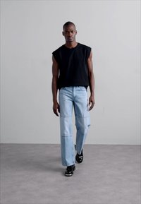 Un top negru fără mâneci, asortat cu blugi de culoare albastru deschis, cu cusături patchwork și o croială lejeră, completat cu pantofi negri.