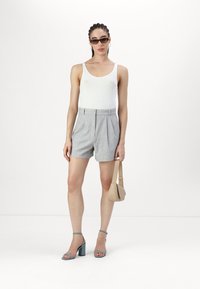 Gray high-waisted shorts with pleats, paired with a white tank top. Accessories include a beige bag and blue ankle strap heels.