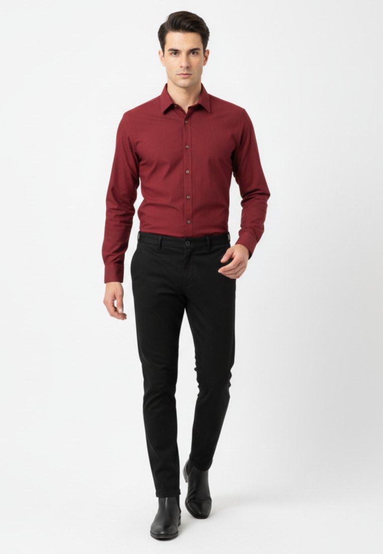 Joven caminando hacia adelante con una camisa de botones ajustada en color burdeos, pantalones negros ajustados y zapatos de vestir negros, sobre fondo blanco.