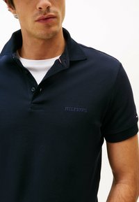 Navyblauwe polo met een gestructureerde stof, voorzien van een kraag met twee knopen, subtiele geborduurde "HILFIGER"-logo en contrasterende rode en witte accenten.
