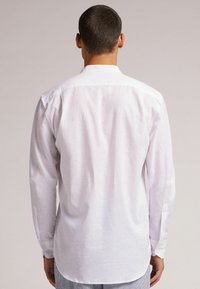 Camisa blanca de manga larga en un tejido ligero y texturizado. Cuenta con un collar clásico, puños con botón y un dobladillo recto.