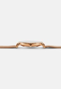 Montre en ton or rose avec un boîtier rond et mince, un verre en verre et un bracelet en maille. Le bracelet présente un tissage complexe et une texture lisse.