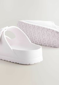 Vita slip-on sandaler med öppen baksida, texturerad rem och mönstrad sula. Tillverkade av lättviktigt material med en slät yta.