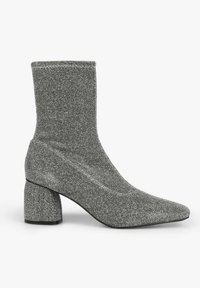 Bottine argentée à paillettes avec un talon bloc et un bout arrondi, dotée d'une tige extensible façon chaussette et d'une semelle lisse.