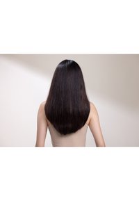 De longs cheveux noirs raides tombent jusqu'aux épaules, vus de dos. L'arrière-plan est clair avec des ombres subtiles, et la personne porte un haut beige.