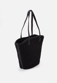 Svart toteväska gjord av fluffigt texturerat material med släta läderdetaljer, med långa handtag och design utan lock.