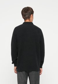 Zwarte gebreide trui met een gestructureerd patroon, voorzien van een kraag, lange mouwen en een relaxte pasvorm, gecombineerd met geruite broek.