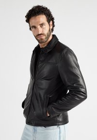 Zwart leren jasje met een klassieke kraag, ritssluiting en zijzakken. Glad oppervlak en een getailleerd ontwerp. Draag over een zwart shirt.