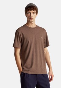 T-shirt a maniche corte marrone realizzato in tessuto misto cotone, con scollatura a girocollo e un piccolo logo ricamato sul lato sinistro.