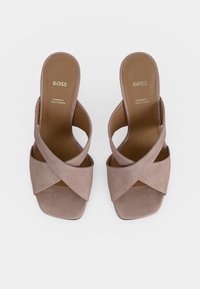 Paire de sandales taupe en daim à brides croisées et bout ouvert carré avec logo BOSS sur la semelle intérieure, présentées sur fond blanc.