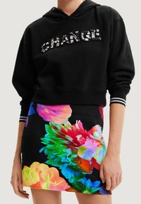 Czarna krótka bluza z kapturem z metalicznym napisem "CHANGE", zestawiona z dopasowaną mini spódniczką w żywe kwiatowe wzory na ciemnym tle.